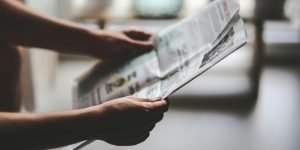 Hands holding a newspaper in a soft-lit, indoor environment, focusing on a relaxed reading moment.