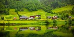 Tranquil countryside scene with houses reflected in a calm river.