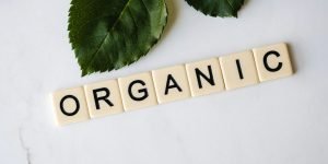 Close-up of 'ORGANIC' spelled with tiles next to a leaf on a marble surface.