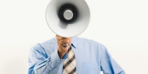 Businessman in blue shirt holding megaphone, symbolizing leadership and communication.